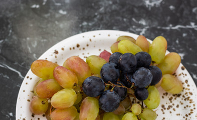 Assortment summer grapes in a plate on dark marble background
