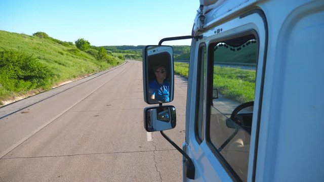 Trucker in sunglasses reflecting in side mirror of moving car. Man driving lorry riding to destination through countryside road. Cargo transportation concept. Beautiful background. Slow mo Close up