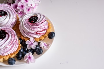 Sweet tartlet with meringue and blueberry and huckleberry jam and phlox flowers on white background closeup