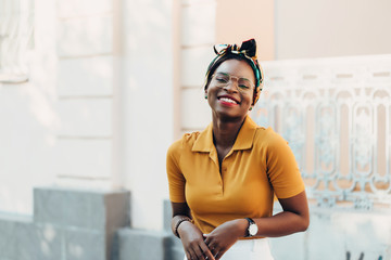 Elegant black girl with glasses and a colored bandage on her head on the city streets.