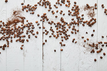 White wooden surface with scattered coffee beans and ground coffee