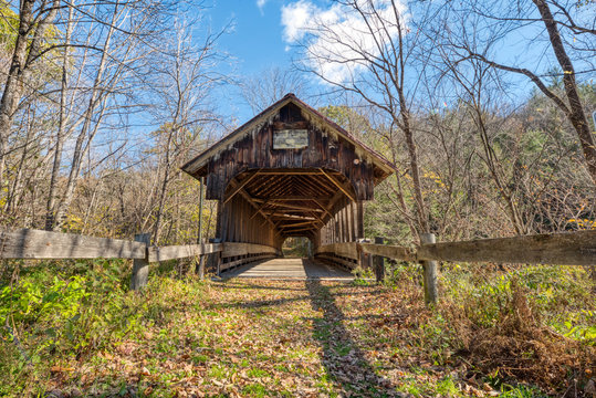 A covered bridge, long abandoned, still stands in the countryside despite being neglected with weathered wood.