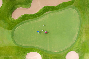 Aerial view of players on a green golf course. Golfer playing on putting green on a summer day.