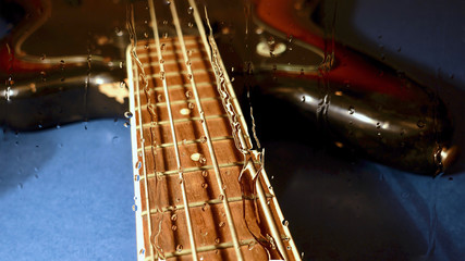 bass guitar behind the glass with water drops . color background