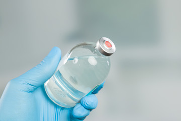 doctor's hand in medical gloves holding a a serum flask