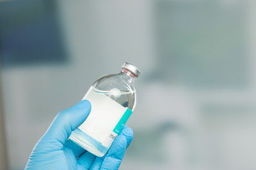 doctor's hand in medical gloves holding a a serum flask