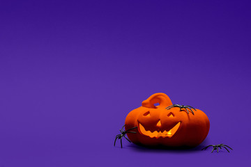 Carved Halloween pumpkin, jack o lantern with spiders on it on a blue  background with copy space and room for text