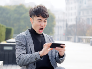 Happy excited young man in suit using cell phone with funny expression, excited business man looking at his smart phone reading good news message email, emotional lifestyle concept.