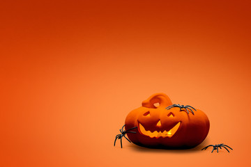 Carved Halloween pumpkin, jack o lantern with spiders on it on an orange background with copy space and room for text