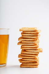 A stack of golden wheat cookies and a mug of fragrant green tea in on a white background. Cookies laid out in a breakfast column and a golden highlight with tea mugs
