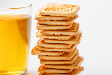 A stack of golden wheat cookies and a mug of fragrant green tea in on a white background. Cookies laid out in a breakfast column and a golden highlight with tea mugs