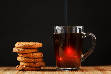 Oatmeal cookies with pieces of chocolate and a mug of coffee on a bamboo stand.