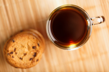 Oatmeal cookies with pieces of chocolate and a mug of coffee on a bamboo stand. Close-up