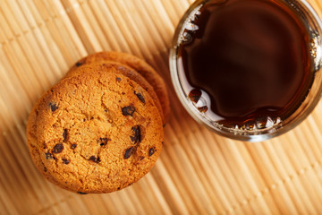 Oatmeal cookies with pieces of chocolate and a mug of coffee on a bamboo stand. Close-up