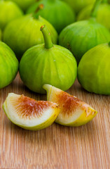 Whole and cut green figs, with fig leaves. Foreground. On wooden background.