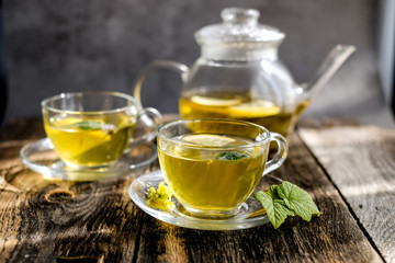 Herbal tea with lemon and honey in glass cup and teapot on sunny day light