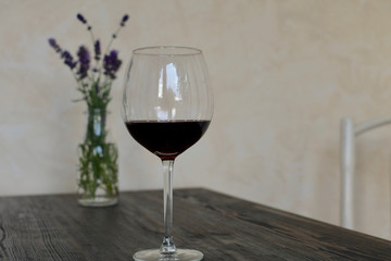 one glasse of red wine on wooden table vase in background