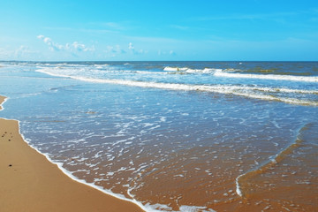 Sanfte Welle am goldenen Sandstrand mit blauem Wasser und blauem Himmel.