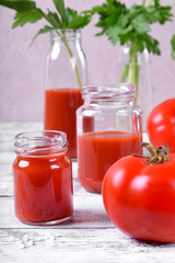 Tomato juice in glass jars on white wooden table