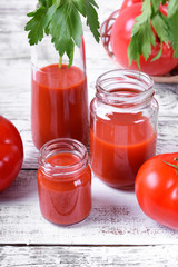 Tomato juice in glass jars on white wooden table