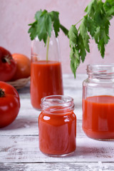 Tomato juice in glass jars on white wooden table