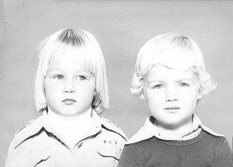 Monochrome 1978 portrait of a side-eyeing girl with blond hair and a boy with blond hair looking at...