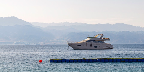 a small white yacht is anchored in the gulf of eilat akaba in israel with the mountains of jordan in a hazy background
