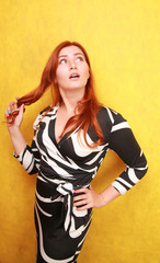 pretty red-haired adult caucasian girl in black and white spandex tight dress on yellow studio background alone