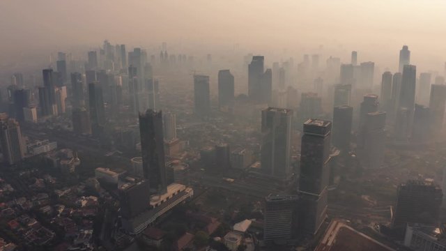 JAKARTA, Indonesia - August 27, 2019: Aerial footage of air pollution fog around office buildings in business district on the morning. Shot in 4k resolution from a drone flying forwards