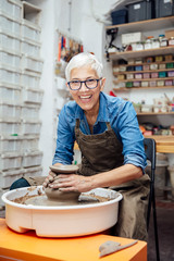 Senior female potter working on pottery wheel while sitting  in her workshop