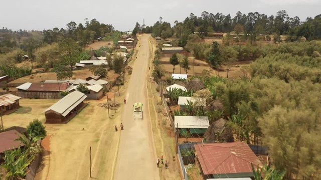 Drone flight of passenger bus driving over unpaved dirt road through small village community of Dorze, infrastructure and public transport in Ethiopia Africa
