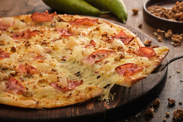 Tasty freshly prepared pizza with pear, nuts and bacon on a wooden board, rustic style