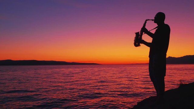 saxophonist plays against the backdrop of a beautiful sunset and the sea