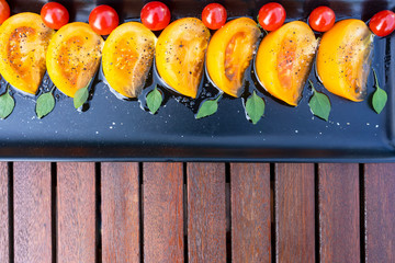 Red cherry tomatoes and yellow tomato slices are sprinkled with unfiltered olive oil, topped with basil. Served in a black plate on wooden table. 