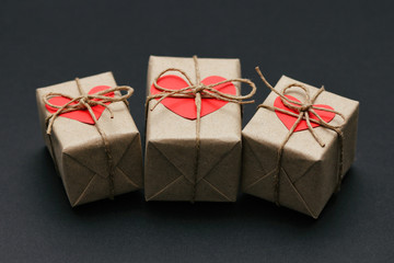 Set of gift boxes on black background. Heart cardboard. Parcels wrapped in craft paper and tie hemp cord.