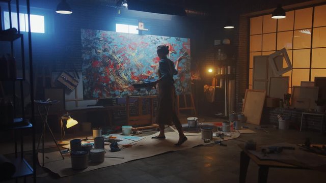 Talented Female Artist Working on a Modern Abstract Oil Painting, Uses Splattering and Dripping with Paint Brush Technique. Dark Creative Studio Large Picture Stands on Easel Illuminated. Slow Motion