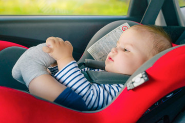 Portrait of cute toddler boy sitting in car seat. Child transportation safety concept.