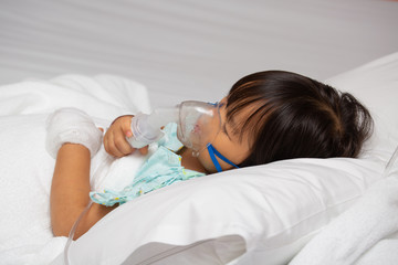 Little Asian girl is sick in a bed with an oxygen mask in hospital
