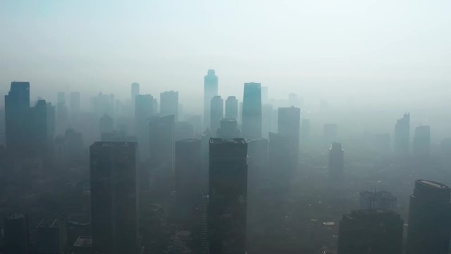 JAKARTA, Indonesia - August 27, 2019: Aerial view of silhouette of skyscrapers with dense air pollution haze in business district on the morning. Shot in 4k resolution from a drone flying forwards