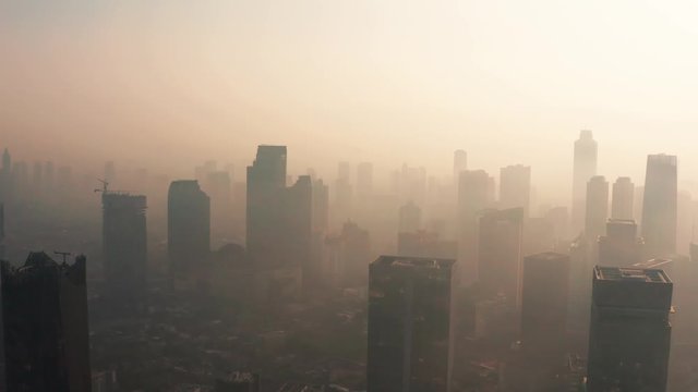 JAKARTA, Indonesia - August 27, 2019: Aerial view of unhealthy business district with silhouette of skyscrapers and dense air pollution haze. Shot in 4k resolution from a drone flying forwards