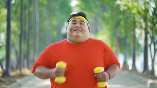 Attractive overweight young man doing workout by running at the park while holding dumbbells for losing weight. Shot in 4k resolution