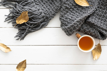 Autumn composition. Feminine desk table with knitted scarf, tea cup, fall leaves on wooden white background. Flat lay, top view. Nordic, hygge, cozy home concept