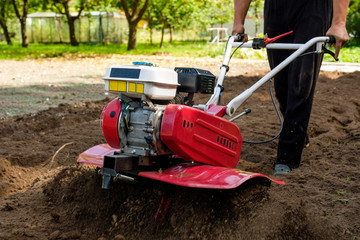 Man working in the garden with garden tiller machine. Garden tiller to work, close up