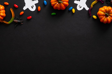 Halloween composition with pumpkins, ghosts, candy on black background. Halloween party invitation card mockup. Flat lay, top view, copy space.