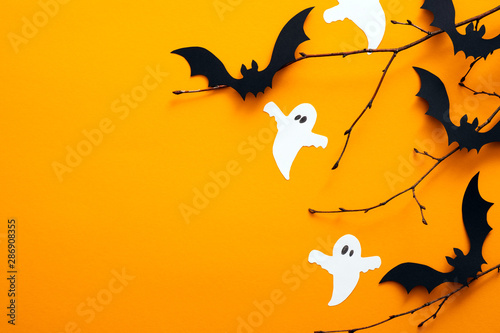 Happy halloween holiday concept. Halloween decorations, bats, ghosts on orange background. Halloween party greeting card mockup with copy space. Flat lay, top view, overhead.
