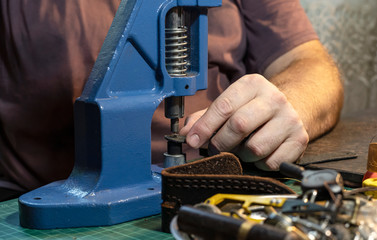 A man works with a press to install accessories on leather products.
