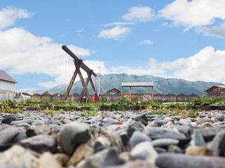 A playground in the yard with a swing made of wood against a picturesque landscape with mountains and a blue sky and clouds.