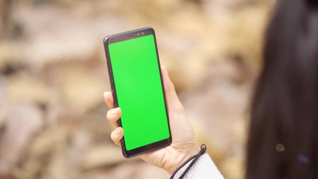 Closeup of woman hand holding a mobile phone with empty green screen at the autumn park. Shot in 4k resolution