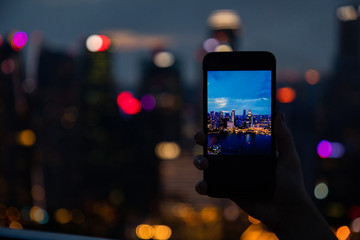 Woman hand holding a phone and taking a picture of the skyline views from Singapore luxury hotel rooftop