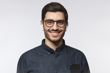 Portrait of young smiling man  listeting to his favorite music track with earphones, wearing blue denim shirt and eyeglasses